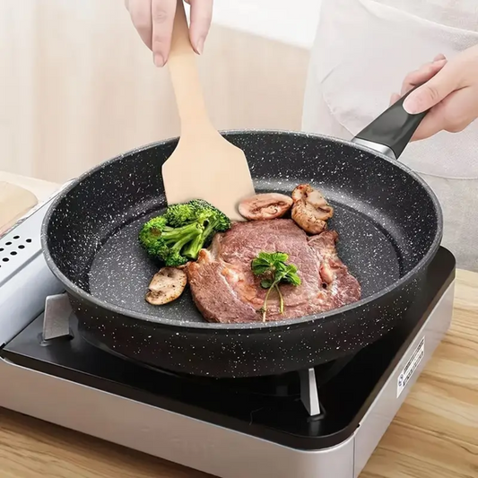 Zwarte anti-aanbak koekenpan van 26 cm met marmercoating op kookplaat, met vlees en groenten erin.